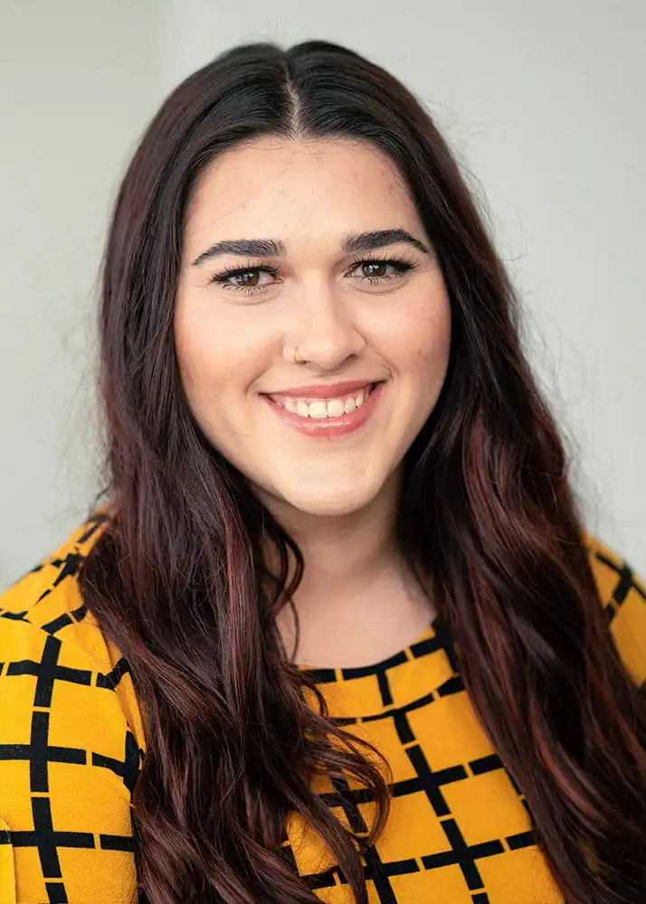 A portrait photo of the friendly office manager at Yard Master Services. She has brunette hair and is wearing a striped mustard colored shirt.