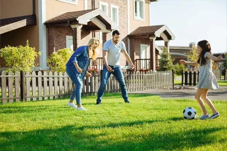 A happy family plays on a lush green lawn in front of their house.